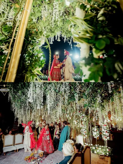 The couple at their mandap, which is adorned with hanging white flowers, creating a dreamy and romantic atmosphere for their pheras.