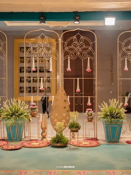 A beautiful and intricate entrance decor setup. The use of turquoise, gold, and pink, along with traditional elements like hanging flowers and brass art, creates a welcoming and artistic foyer.