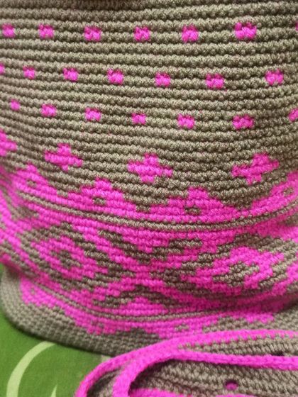 A work-in-progress shot of a tapestry crochet backpack. You can see the geometric pink pattern emerging against the brown background, a technique that creates durable and graphic designs.