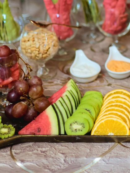 A beautifully carved and sliced fruit platter, featuring watermelon, kiwi, and oranges. The intricate cuts add a touch of artistry to the display.