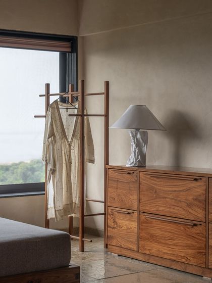 A quiet corner of the bedroom, where a custom clothing rack and console table provide simple, functional storage. The large window allows for plenty of natural light and a view of the sea.