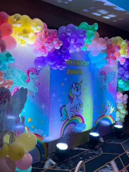 A unicorn-themed party with a vibrant, UV-lit backdrop. The neon colors of the balloons and unicorn illustrations create a magical, glowing effect.