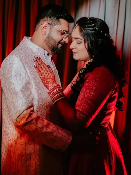 A tender moment captured during an engagement. The bride's hands, adorned with henna and bangles, rest on her partner's chest in this beautiful, emotional photograph.