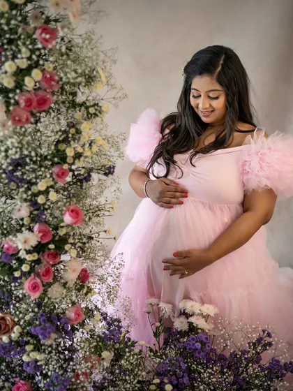 A quiet moment of connection. The mom-to-be looks down at her belly with so much love, her pink gown blending beautifully with the floral decor.