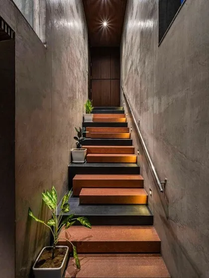 The interplay of raw materials can create powerful designs. We are inspired by staircases that use a simple palette, like the combination of concrete walls, terracotta-colored steps, and subtle step lighting seen here, to create a path that is both moody and beautiful.