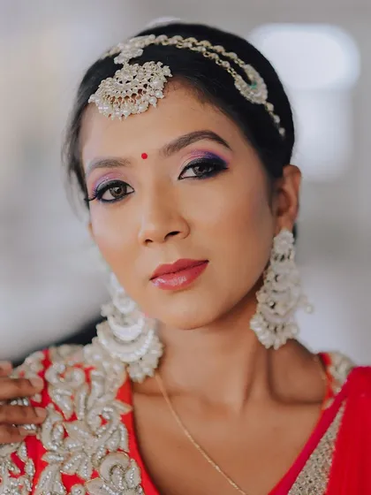 A close-up portrait of a model in a red and silver lehenga. The focus is on her expressive eyes, makeup, and the intricate details of her headpiece.