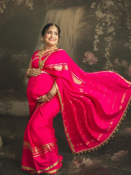 The joy of a mother-to-be in a vibrant pink saree. The flowing fabric and the artistic backdrop with a waterfall and swan come together to create a truly magical, painting-like effect.