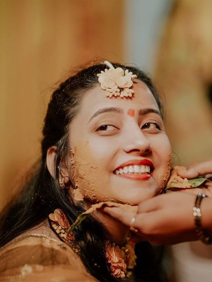 A beautiful, candid close-up of the bride smiling as Haldi is applied to her face. Her genuine happiness shines through in this shot.