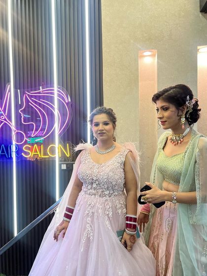 Two clients ready for a party. One is in a pink gown and the other in a pastel green lehenga, both with makeup and hair done by our team.