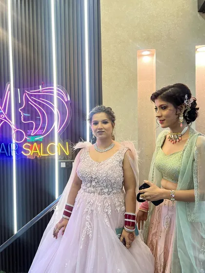 Two clients ready for a party. One is in a pink gown and the other in a pastel green lehenga, both with makeup and hair done by our team.