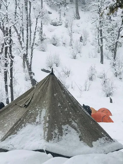 A close-up of the snow-dusted canvas tent, showing its resilience in the winter forest. This type of shelter offers a different, more traditional camping feel.