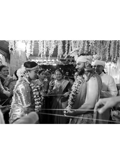 A black and white shot of a South Indian wedding ceremony. The couple gazes at each other during a ritual, surrounded by family, in a moment of deep connection.