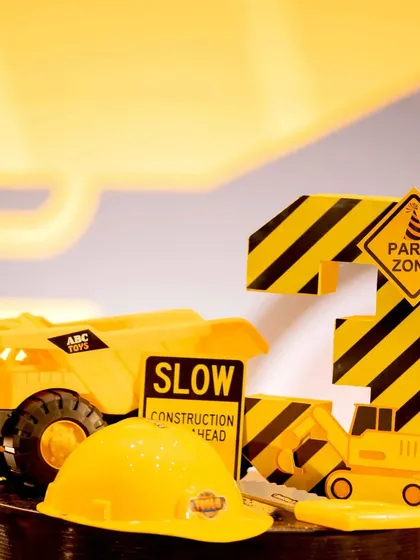 A close-up of a tabletop decoration for a third birthday. It features a toy dump truck, a mini hard hat, and a custom-made number '3' with construction stripes, showing my attention to even the smallest details.