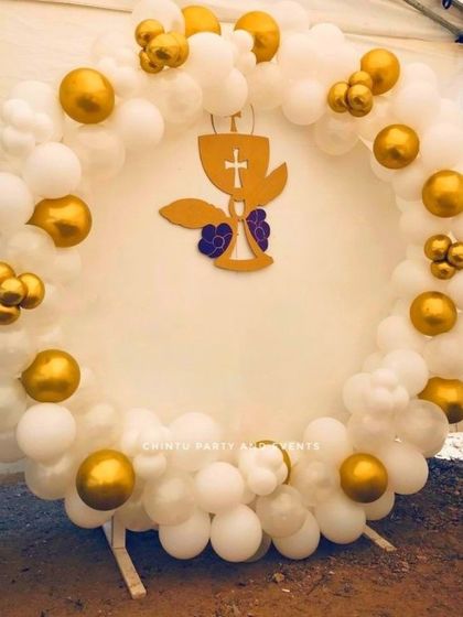 An outdoor baptism ceremony decoration with a white and gold balloon ring. A cutout of the holy chalice is placed in the center.