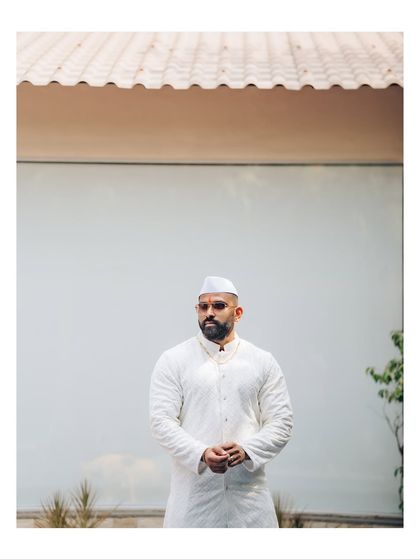 A minimalist and powerful portrait of the groom in traditional white attire. The clean background and simple composition make for a striking image.