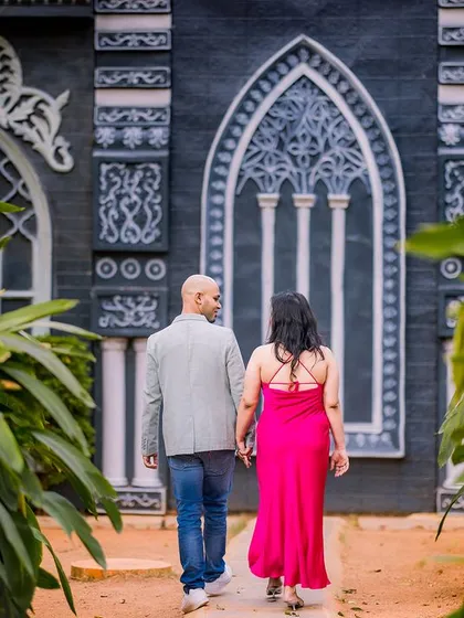 A couple walks away hand-in-hand from a gothic-style black and white building, creating a moody and romantic scene.