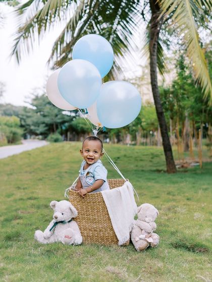 A smiling baby in a hot air balloon basket, surrounded by teddy bears. This is a classic and heartwarming setup for a first birthday.