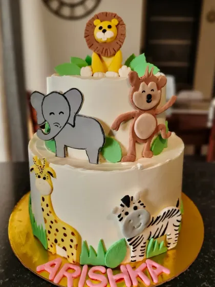 Welcome to the jungle! This two-tier cake is perfect for an animal themed party. It features hand-drawn and fondant animal figures like a giraffe, zebra, elephant, and monkey, all ready to celebrate. I love creating these playful scenes on a cake.