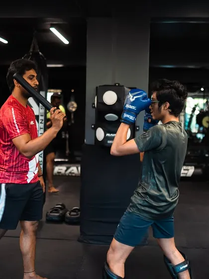 A coach guides a student through a defensive drill, using striking sticks to simulate incoming attacks and improve blocking.