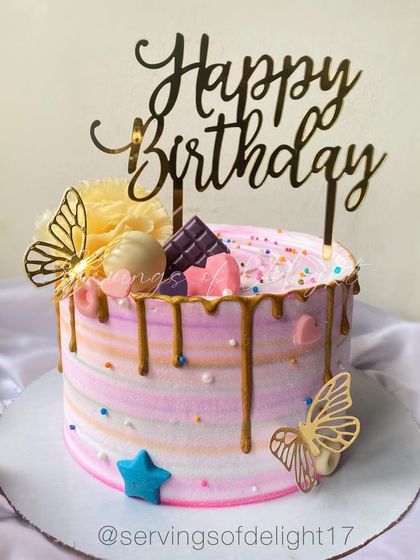 A lovely pastel-striped birthday cake with a gold drip and butterfly accents. The colors are soft and dreamy, perfect for a special celebration.