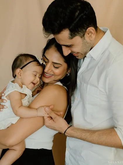 A beautiful, candid moment captured in the studio. The parents gaze lovingly at their smiling baby girl, creating a portrait that is overflowing with tenderness and affection.
