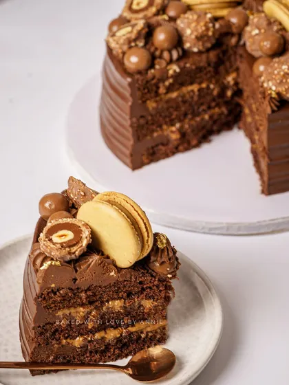 A slice of luxury. This cake features a moist dark chocolate sponge, 54% Belgian dark chocolate ganache, and a crunchy blend of hazelnut praline feuilletine, topped with Ferreros and macarons.