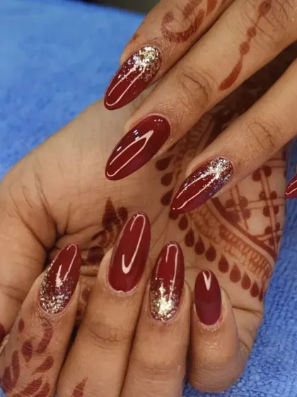 A rich maroon polish on almond-shaped nails, paired with a brilliant gold glitter accent nail for a luxurious contrast.