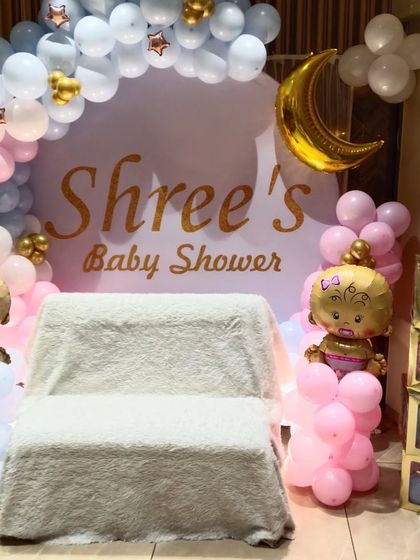 A lovely baby shower balloon decoration for a home party. The setup includes a circular backdrop, 'BABY' blocks, and character foil balloons in a pink and blue color scheme.