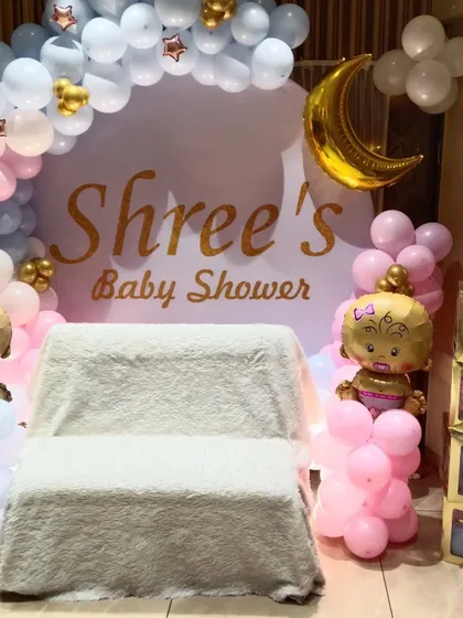 A lovely baby shower balloon decoration for a home party. The setup includes a circular backdrop, 'BABY' blocks, and character foil balloons in a pink and blue color scheme.