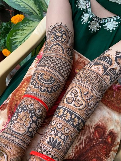 A close-up of the arm portion of a bridal design, featuring peacocks, diyas, and architectural domes.