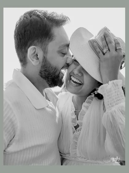 A playful and intimate black and white portrait. The hat adds a touch of fun and spontaneity, capturing a genuine moment of laughter and affection during their outdoor pre-wedding session.