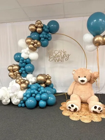 A minimalist and modern teddy bear setup with a golden ring backdrop. The teal, white, and gold balloon garland and jute rug create a chic and stylish look.