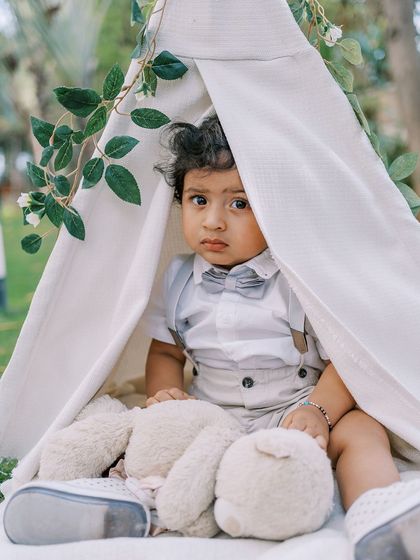 A baby boy peeking out of a teepee during his first birthday shoot. Props like these encourage play and create adorable photo opportunities.