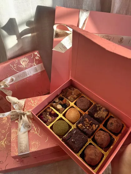 This is my Truffle Edition box, which includes my handmade dark chocolate truffles alongside the brownies and blondies. The sunlight here really shows off the beautiful pink and gold foil packaging.