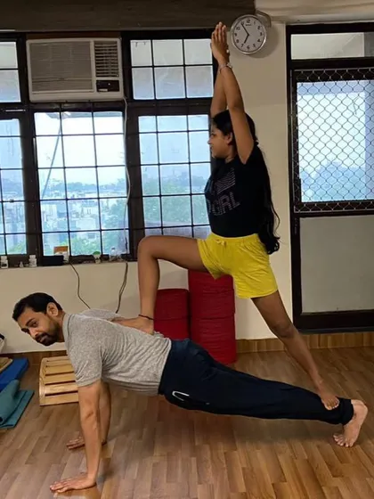 In this partner pose, I demonstrate a plank, providing a stable base for the student's warrior pose. This variation builds immense core strength for the base and balance for the flyer.