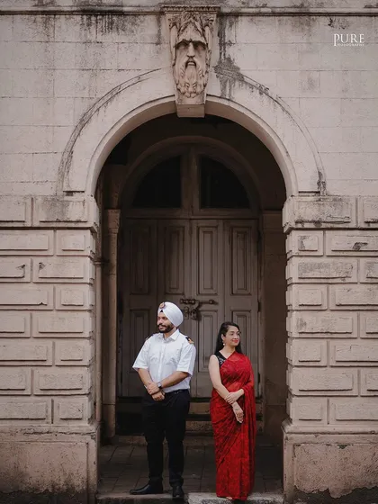 A formal portrait of Kanwaldeep and Avneet standing under a grand archway in Mumbai. The architectural details and their poised stance give this pre-wedding photo a touch of classic elegance.