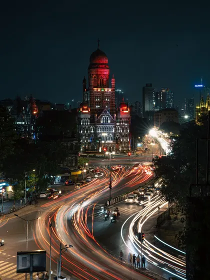 A long-exposure shot of Mumbai's Municipal Corporation Building at night, with light trails from traffic creating rivers of light. This image shows the city's constant motion, a blend of historic architecture and relentless modern energy.
