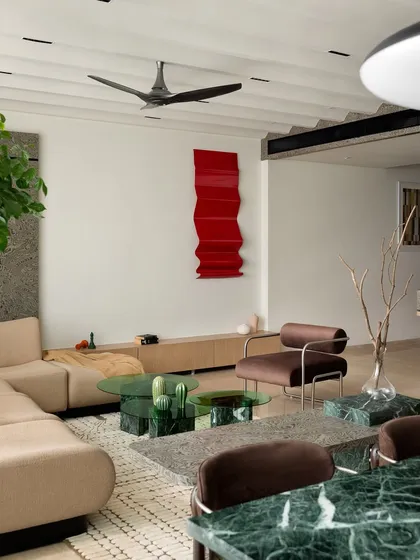 The living room of 'ARAH', featuring a custom 16-foot bouclé sofa, a bespoke armchair, and a green glass and marble coffee table. The varied seating styles create a distinctive yet cohesive look.