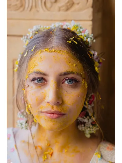A close-up portrait of a bride after her haldi, her face covered in turmeric and her blue eyes shining through. It’s a raw, beautiful, and colorful moment that we love to capture.