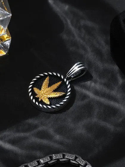 A cool and edgy shot of a cannabis-leaf pendant, styled with a glass of whisky and dark shadows to create a party-ready vibe.