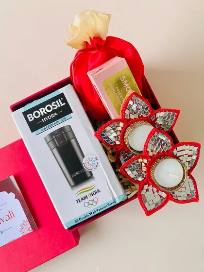 This red gift box includes a practical Borosil coffee mug, along with festive mirror-work T-light holders and a satin potli with treats.