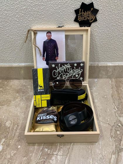 The final look of the wooden birthday box hamper for him. It includes a wallet, belt, sunglasses, chocolates, and a personal photo, making it a complete and thoughtful gift.