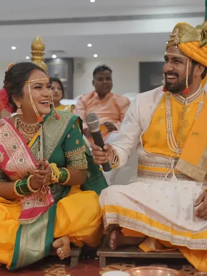 Capturing the fun and games of a Maharashtrian wedding. The groom speaks into a microphone, sharing a laugh with his bride and the guests.