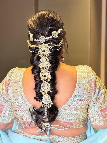 A messy braid adorned with a beautiful ornament. This is a great hairstyle for a sangeet or mehendi, combining traditional elements with a modern, relaxed feel.