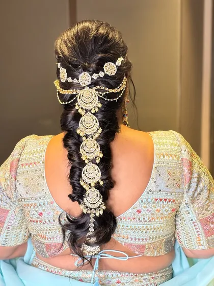 A messy braid adorned with a beautiful ornament. This is a great hairstyle for a sangeet or mehendi, combining traditional elements with a modern, relaxed feel.