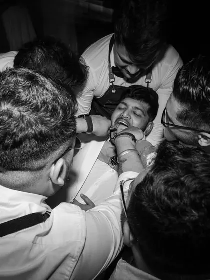 A raw, candid moment from an after-party. This black and white shot captures the fun and chaos of friends celebrating with the groom, a memory they'll laugh about for years.