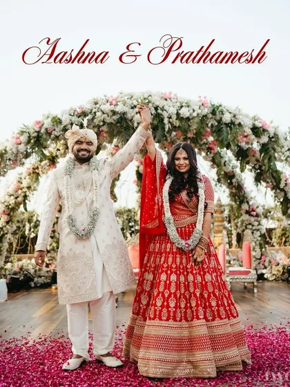 The "just married" feeling! The couple raises their hands in victory after the varmala, under a beautiful floral arch, with petals raining down on them. A picture of pure happiness.