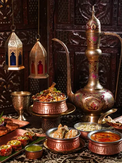 A grand Awadhi feast featuring biryani, korma, and kebabs, styled with antique brass lanterns and an ornate jug. This shot captures the grandeur and richness of a traditional Lucknowi dastarkhwan.