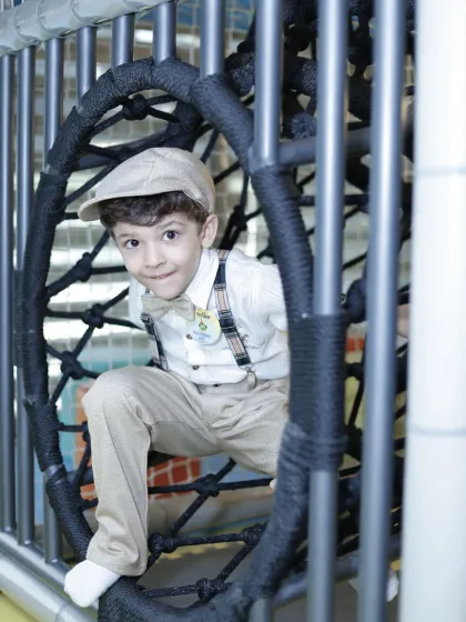 A dapper young man peeks through a netted climbing wheel in our play maze.