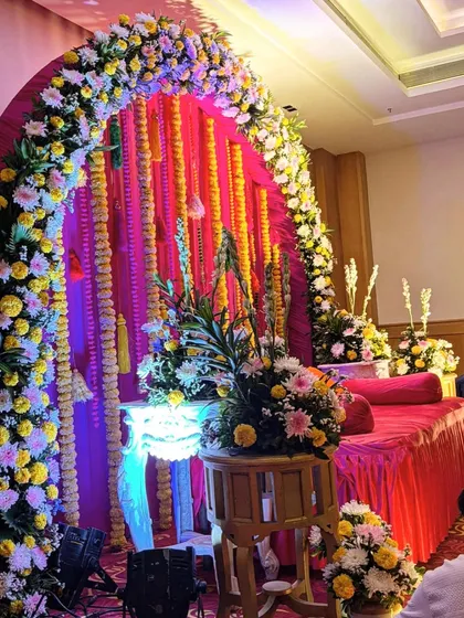 A colorful indoor setup for a pre-wedding ritual. The arch is decorated with a mix of fresh flowers and marigold strings, creating a festive and traditional look.